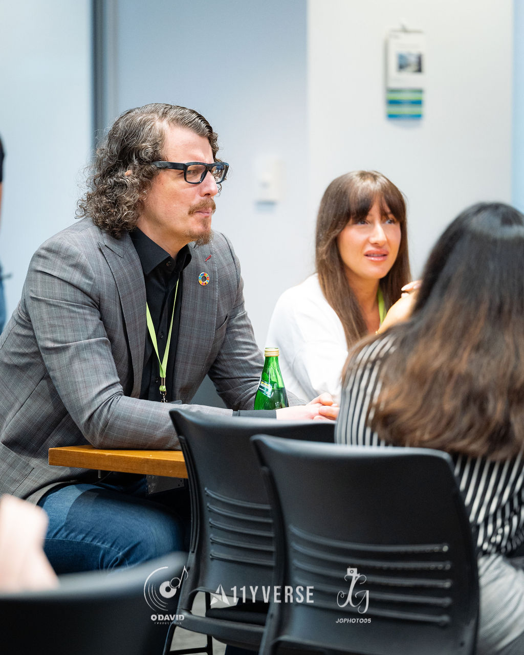 A small group seated in a discussion circle, one person leaning on a high table and listening intently while the others around them follow the conversation.