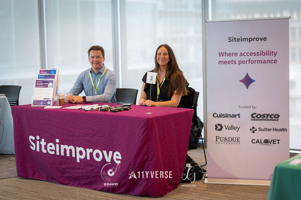 Two people sit smiling behind a Siteimprove booth with a magenta cloth, beside a banner reading where accessibility meets performance, with brochures and devices on the table.